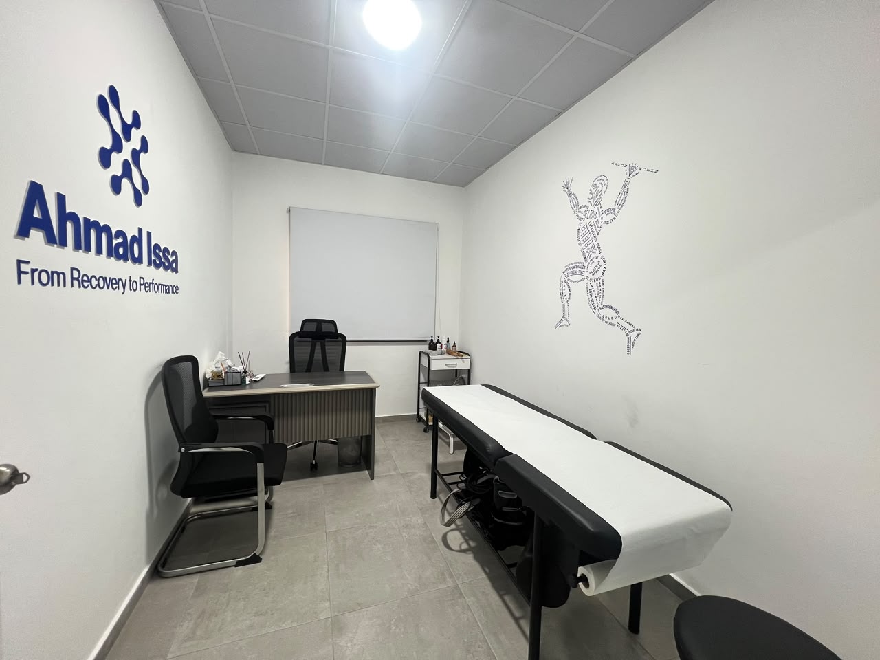 Consultation room with Ahmad Issa clinic signage, desk, seating and examination couch